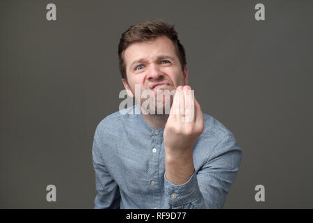 Junger stattlicher Mann mit italienischen Geste das bedeutet was wissen Sie über die grauen Hintergrund wünschen Stockfoto