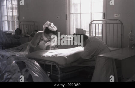 1950, historische, zwei weibliche Krankenschwestern in einem Krankenhaus, mit neuen Bettwäsche oder Blätter auf einer Matratze auf einem metallischen Bett, England, UK. Stockfoto