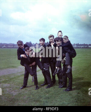1962, historische Gruppe britischer Teenager Schuljungen in Uniform, Spaß zusammen in einem Feld oder Park, der von ihrer Schule, Liverpool, England, UK, mit zwei der Jungen auf Huckepack. Stockfoto