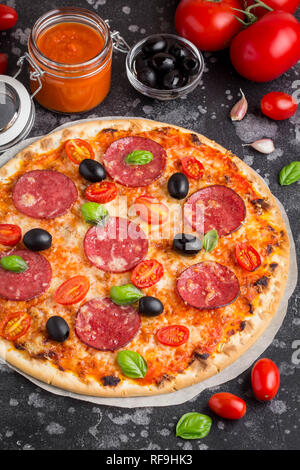 Italienische Pizza auf dünnem Teig mit Tomatensauce, Salami, Käse, Oliven und Basilikum Stockfoto