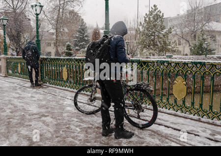 Der junge Mann ist Kontrolle ihres Telefons unter Schneefall in der Stadt. Stockfoto