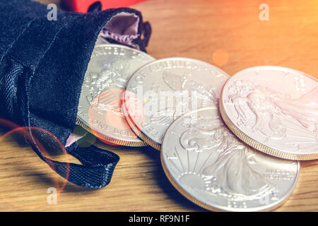 Nahaufnahme von Silbermünzen amerikanischen eine Unze Adler und Ziegel aus schwarzem Geld Tasche fallen und Festlegung auf hölzernen Hintergrund Stockfoto