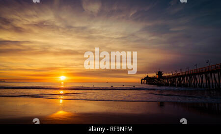 Die untergehende Sonne am Pier in Imperial Beach, Kalifornien mit Surfer schwimmen Wellen zu fangen. Stockfoto