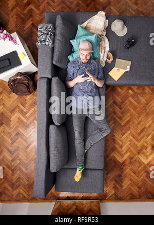 Ein junger Hippie, Verlegung in Couch in seinem Zimmer. mit Smartphone. Bird's Eye View; Blick von oben. Stockfoto