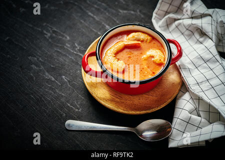 Traditionelle thailändische Suppe mit Garnelen und Kokosmilch in einem roten Topf und Löffel Stockfoto