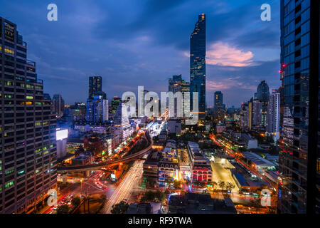 Bangkok, 12.11.18: Stadtbild der berühmten Maha Nakhon Tower in Bangkok, Thailand. Leichte Wanderwege in den Straßen von den Autos. Schönen Sonnenuntergang in den Himmel hinter Türme der Stadt. Stockfoto