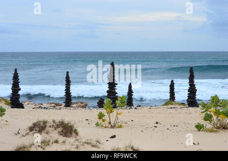 6 Cairns aus schwarzen vulkanischen Kieselsteinen am Strand an der südlichen Küste der Insel Boa Vista, Kap Verde Inseln, Afrika. Stockfoto