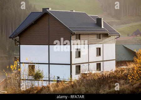 Neue schöne weiße und braune zweistöckiges Ferienhaus mit Schindeldach im ökologischen Bereich auf nebligen Wald und Hügel Hintergrund auf sonnigen Sommertag. Auch maintai Stockfoto