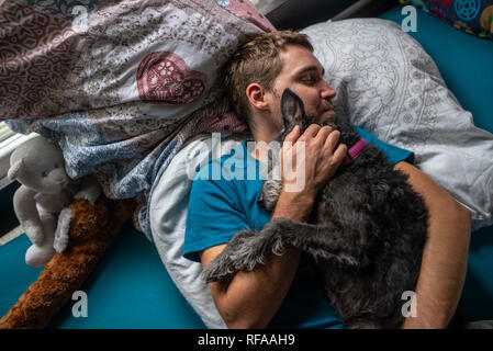 Blick von oben auf die jungen Mann schlafend in seinem Bett kuscheln mit seinem Hund liegen oben auf ihm. Stockfoto