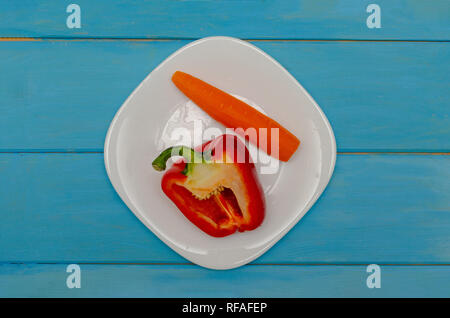 Bulgarischen roten Pfeffer mit Karotten auf einem weißen Teller. Holz- blauen Hintergrund. Das Konzept der gesunden Ernährung Stockfoto