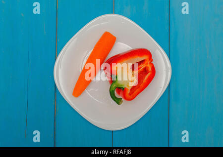 Bulgarischen roten Pfeffer mit Karotten auf einem weißen Teller. Holz- blauen Hintergrund. Das Konzept der gesunden Ernährung Stockfoto