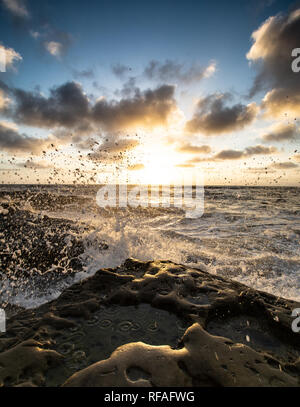 Wellen, die auf einem felsigen Strand bei Sonnenuntergang Stockfoto