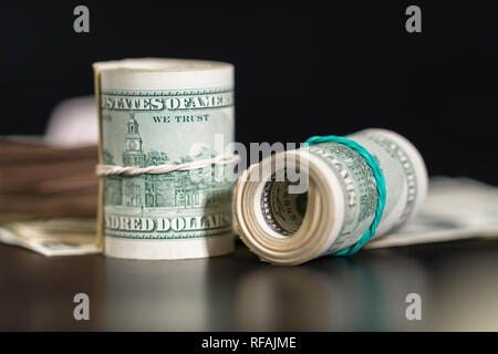 Zwei Bündel von Amerikanischen Dollar Banknoten an einem reflektierenden schwarzen Tisch in einem Low Angle View für finanzielle Konzepte Stockfoto