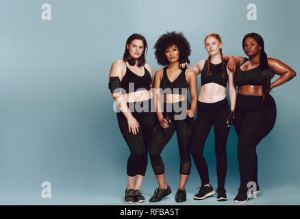 Volle Länge des multi-ethnischen Frauen mit in Sportkleidung zusammen über grauer Hintergrund stehen. Drei Frauen unterschiedlicher Rasse, Abbildung Art und Größe in f Stockfoto