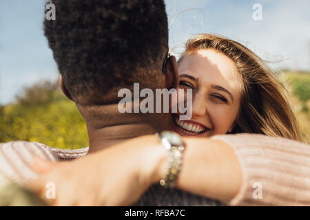 Fröhliche Frau ihrem Freund umarmen. Romantische interracial Paare im Freien. Stockfoto