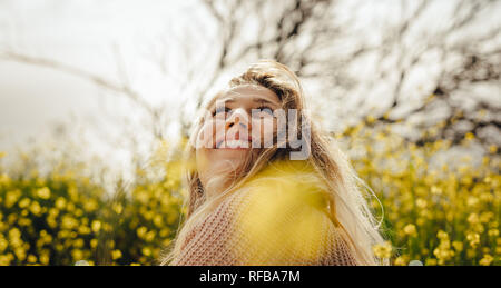 Nahaufnahme von lächelnden jungen Frau sitzt in der Wiese mit gelben Blumen im Freien. Kaukasische weiblichen weg schauen und lächeln. Stockfoto