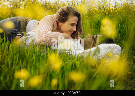 Wunderschöne liegende Frau mit ihrem Freund auf dem hohen Gras. Junge Paare, die auf dem Gras in der Wiese. Stockfoto