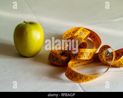 Adipositas Konzept. Ein grüner Apfel und ein Maßband auf einem Tisch Stockfoto