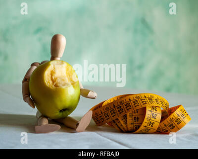 Eine hölzerne Figur mit einem grünen Apfel gebissen und ein Maßband, auf einem Tisch Stockfoto