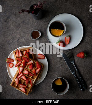 Leckere Belgische Waffeln mit frischen Erdbeeren am weißen Platte und zwei Tasse Tee mit Zitrone auf dunklem Hintergrund. Konzept der gesunden Lebensstil für Menü Stockfoto