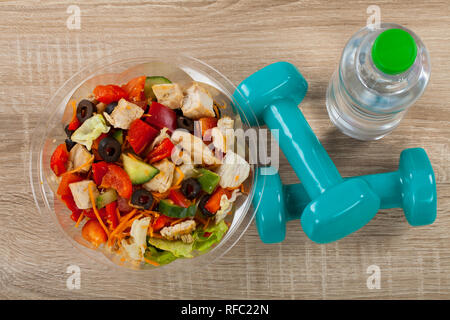 Nahaufnahme Bild einer frischen Chicken Salat, eine Flasche stilles Wasser und Kurzhanteln auf hölzernen bakcground. Fitness. Diät. Gewichtsverlust Stockfoto