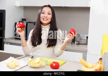 Bild von Happy brunette mit Pfeffer in der Hand am Tisch mit Gemüse und Obst in der Küche Stockfoto