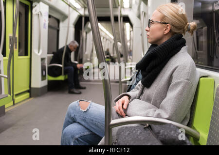 Schöne blonde Frau mit Winterjacke und Schal mit der U-Bahn reisen. Mit den öffentlichen Verkehrsmitteln. Stockfoto