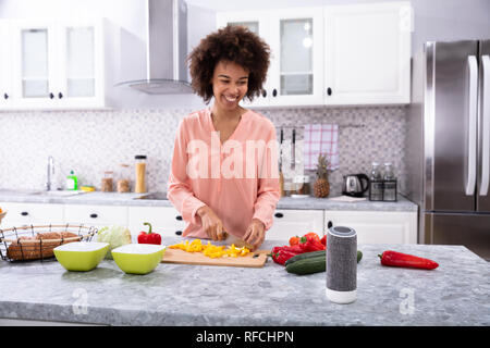 Junge Glücklich afrikanische Frau Schneiden gelbe Paprika auf Schneidebrett in der Küche Stockfoto
