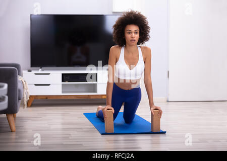 Passen junge Frau mit Holzblöcken während einer Übung auf Yoga Matte im Wohnzimmer Stockfoto