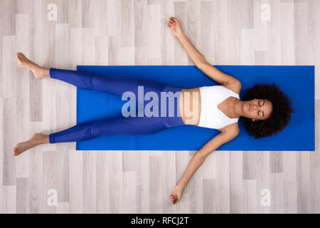 Athletische junge Frau liegend auf Blau Yogamatte über das Parkett Stockfoto
