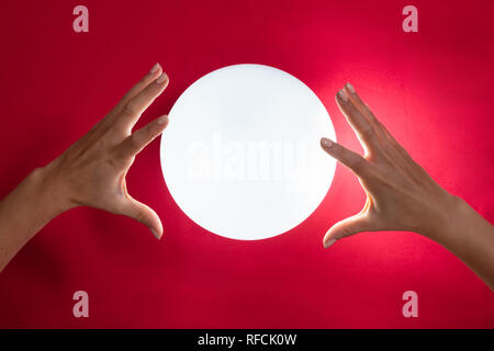 Nahaufnahme der Wahrsager Hand über die glühende Glaskugel Rot Schreibtisch Stockfoto