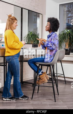 Schöne dunkelhäutige Stylist in beige Stiefel im Gespräch mit einem Kunden Stockfoto