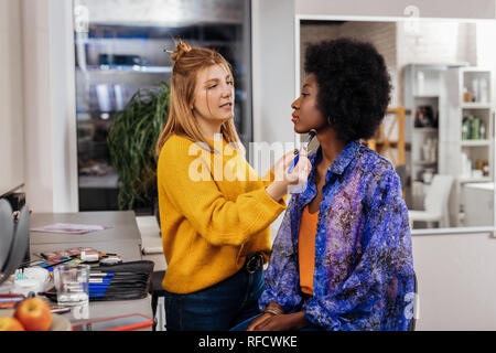 Blonde stylist, make-up, eine hübsche dunkelhäutige Modell Stockfoto