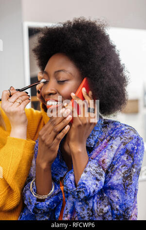 Stylist in einem gelben dicken Pullover, Lidschatten auf Modellen, die Augenlider Stockfoto