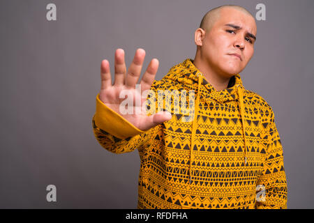 Junge kahle asiatischer Mann gegen grauer Hintergrund Stockfoto