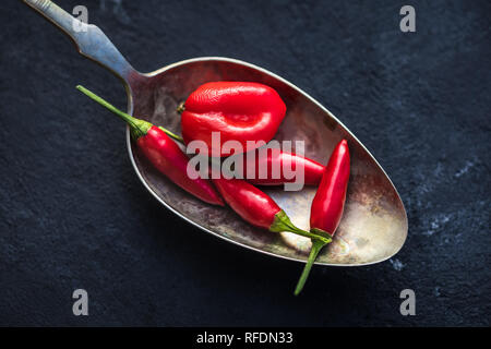 Chili peppers in alten Löffel auf schwarz Tabelle Stockfoto