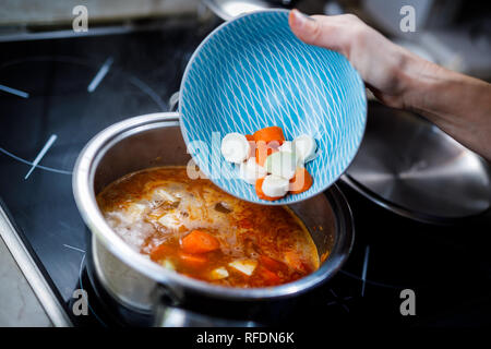 Das zerkleinerte Gemüse in die kochende Gulasch Suppe im Topf gießen Stockfoto