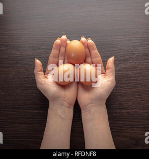 Huhn Eier in weibliche Hände auf hölzernen Hintergrund Stockfoto