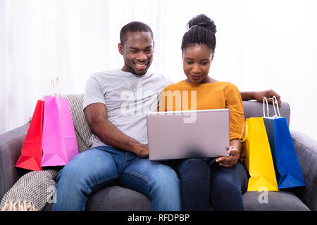 Lächelnden jungen Paar Einkaufen auf dem Laptop in der Nähe der bunten Einkaufstaschen Stockfoto