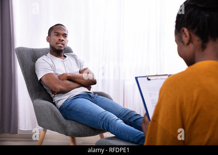 Junge afrikanische Mann sitzt auf Stuhl in der Nähe der Psychologin mit Zwischenablage Stockfoto