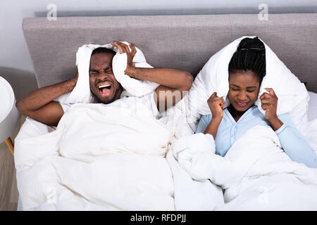 Junge afrikanische Paar durch Lärm gestört, die Ihre Ohren mit Kissen auf dem Bett Stockfoto