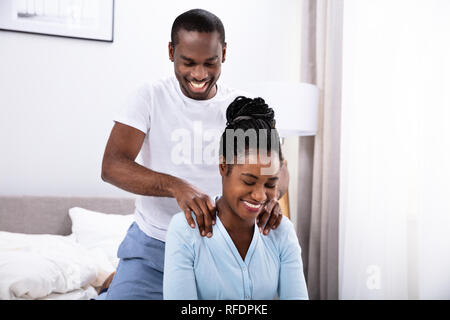 Gerne jungen afrikanischen Mann, der Schulter Massage zu seiner Frau im Schlafzimmer Stockfoto