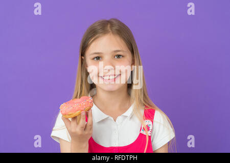 Kind Lächeln mit Donut auf Violett Hintergrund. Kleines Mädchen mit glasierten ring Donut. Glückliches Kind mit Junk Food auf lila Hintergrund. Essen und Nachtisch. Kindheit und Kinderbetreuung. Stockfoto