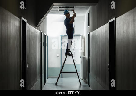 Silhouette eines männlichen Elektriker Leiter Installation Licht im Flur Stockfoto