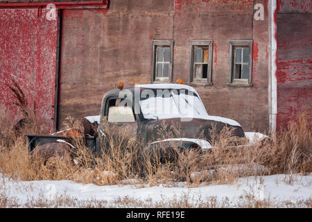 Rostige alte Lkw, mit Schnee, der Windschutzscheibe und orange Lichter auf Kabine, liegt neben dem alten Gebäude, im Winter in den ländlichen Alberta, Kanada. Stockfoto