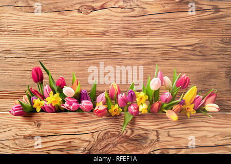 Anordnung der bunten frischen Frühlingsblumen mit Tulpen und Narzissen für Ostern über ein strukturiertes Holz Hintergrund mit attraktiven Holz- und Fantasiedekoren kopieren s Stockfoto