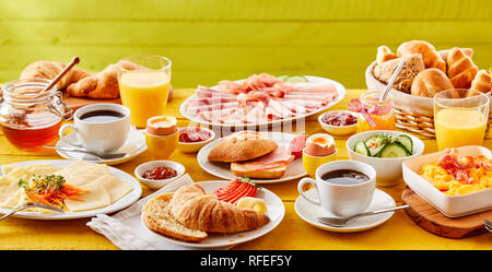 Frühling frühstück Banner mit einer Auswahl von Lebensmitteln, einschließlich einem Croissant, bin oder Speck rollen, Omelette, kaltem Fleisch, Käse, Honig und Marmeladen mit o serviert. Stockfoto