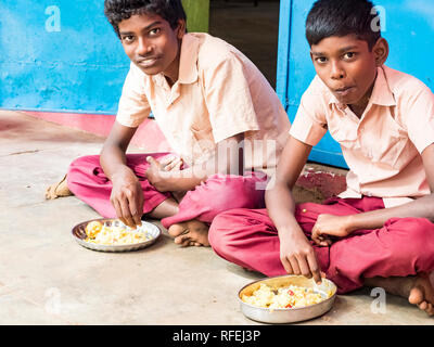 PUDUCHERRY, Tamil Nadu, Indien - Dezember Circa, 2018. Zwei nicht identifizierte armen Mitschüler Jungen mit Uniformen sitzen auf dem Boden im Freien, Essen mit t Stockfoto