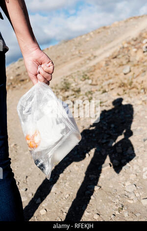 Nahaufnahme von einem jungen Mann in Jeans von hinter einer durchsichtigen Plastikbeutel mit unterschiedlichen Resten wie geht er mit einem trockenen Landschaft gesehen Stockfoto