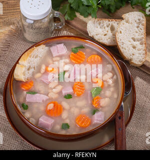 Ansicht von oben aus einer Schüssel Schinken und Bohnensuppe mit Karotten in Scheiben geschnitten und französischem Brot Stockfoto